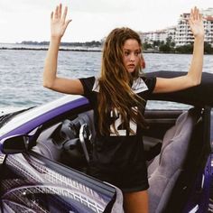 a woman sitting in the driver's seat of a sports car with her hands up