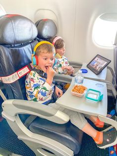 two children sitting in an airplane seat eating cereal