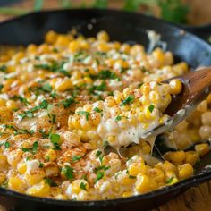 a wooden spoon scooping some food out of a skillet with corn on the cob