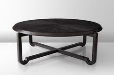 a wooden table with black metal legs and a circular design on the top, sitting in front of a white wall