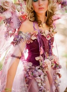 a woman in a pink dress with flowers on her head and wings around her neck