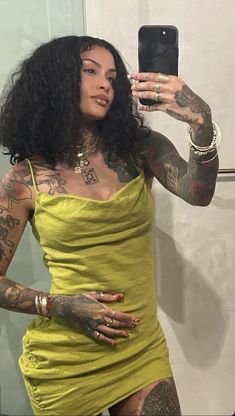 a woman in a yellow dress taking a selfie with her cell phone and tattoos