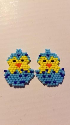 two blue and yellow beaded bird earrings sitting on top of a white table next to each other