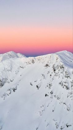 the mountains are covered in snow as the sun is setting over them and pink sky