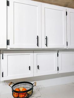 a basket with an orange in it is sitting on the counter next to white cabinets