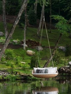 a swing chair hanging from the side of a body of water with trees in the background