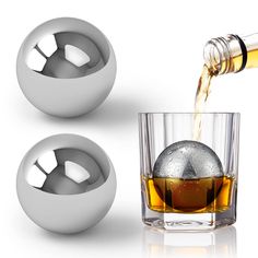 a glass filled with liquid next to two silver balls and a bottle of alcohol on a white background