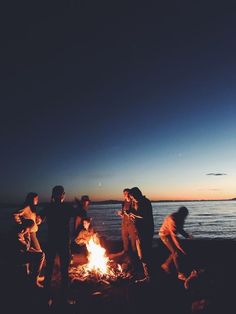 group of people standing around a campfire at the beach