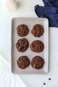 six chocolate cookies on a white plate with milk and blue napkins in the background