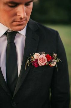 a man in a suit and tie with flowers on his lapel flower is looking down