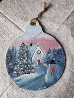 a christmas ornament with a painting of a snowman and a house