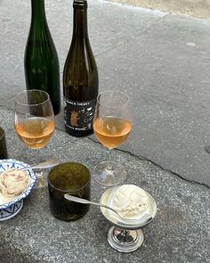 three wine bottles and two glasses with ice cream on the ground next to plates, spoons and bowls