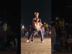 two people dancing on a wooden floor in front of a group of people at night