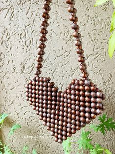 a wooden beaded necklace hanging on a wall next to green plants and leaves in front of a stucco wall