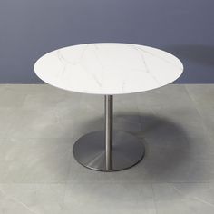 a round white table with a metal base on a tile floor in front of a gray wall