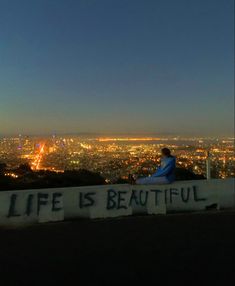 a person sitting on top of a hill with the city lights in the back ground