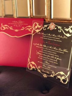 the wedding stationery is set up on top of a black velvet chair with red and gold trimmings