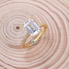 an emerald cut diamond engagement ring on top of a wooden surface with diamonds around it