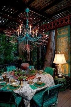 a dining room table set for two with green chairs and chandelier hanging from the ceiling