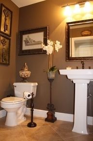 a white toilet sitting in a bathroom next to a sink under a mirror and framed pictures on the wall