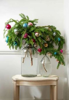 two glass vases with christmas ornaments on top of a table next to a wall