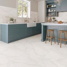 a large kitchen with blue cabinets and white counter tops, two stools in front of the sink