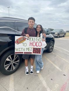 two people standing in front of a car holding a sign that says, you go to hoo with me?