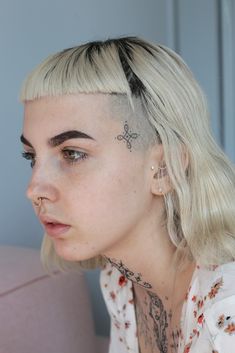 a woman with a cross tattoo on her forehead and behind her ear, looking off to the side