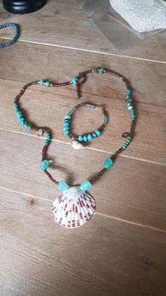 a necklace with a shell and beads is on a wooden table next to a lace doily