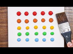 someone is holding a paintbrush and painting different colored buttons on a piece of paper