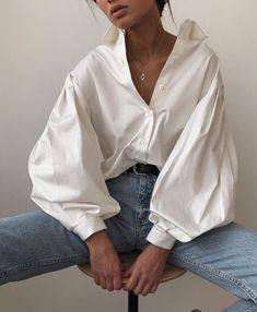 a woman sitting on top of a stool wearing jeans and a white shirt with long sleeves