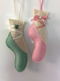 two felt christmas stockings hanging from strings on a white wall with pink and green ribbons