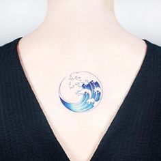 a woman with a tattoo on her chest has a wave in the ocean behind her