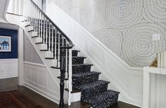 a stair case with black and white designs on the wall, next to a carpeted staircase