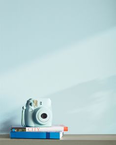 a camera sitting on top of a stack of books next to a blue painted wall