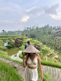 a woman wearing a straw hat walking down a dirt path next to a rice field