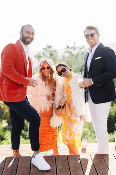 three men and one woman posing for the camera on a wooden deck with trees in the background