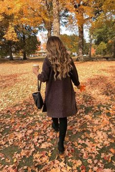 a woman is walking through the leaves with an umbrella in her hand and holding a cup