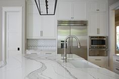 a white kitchen with marble counter tops and stainless steel appliances in the center island area