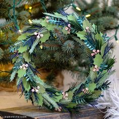 a wreath made out of green paper sitting on top of a wooden table next to a christmas tree