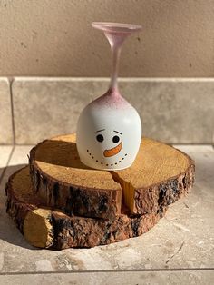 a white and pink vase sitting on top of a piece of wood with a snowman face painted on it