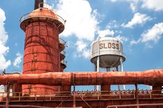 an old rusted pipe and water tower against a blue sky with puffy clouds