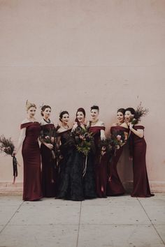 a group of women standing next to each other in front of a pink wall holding bouquets