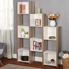 a white book shelf with books on it in a living room next to a window