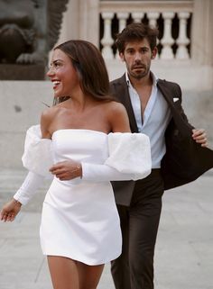 a man and woman are walking down the street in formal wear, one is wearing a white dress