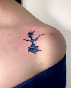 a woman's shoulder with a blue dragon tattoo on her left shoulder and an arrow in the middle