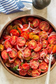 a wooden bowl filled with sliced tomatoes and onions next to a silver serving utensil