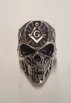 This Sterling Silver Masonic Skull Ring will be an interesting conversation piece for the wearer! We only have a picture of the ring in Sterling Silver, but we are happy to make it in 10k gold, 14k gold, 18k gold or platinum. In addition, the gold can be either yellow gold, white gold, rose gold or green gold (green only available in 14k and 18k. It weighs 41 grams, and is 35x24mm. It sits 10mm above the finger. While puzzle rings are our specialty, we offer a wide range of non-puzzle rings in a Adjustable Skull Rings With Symbolic Style, Symbolic Skull Rings Collectible, Symbolic Engraved Skull Ring, Collectible Symbolic Skull Rings, Symbolic Skull Rings For Halloween, Halloween Skull Rings Symbolic Style, Gothic Skull Rings For Collectors, Gothic Skull Collectible Rings, Symbolic Engraved White Gold Skull Ring