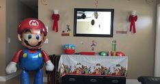 an inflatable mario balloon stands next to a table with toys and decorations on it