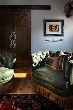 a living room with two green couches in front of a wooden door and rug on the floor